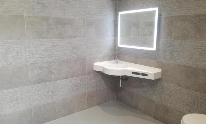 Contemporary bathroom with walk-in shower, grey tiled walls, and illuminated mirror.